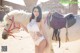 A woman in a white lingerie standing next to a white horse.
