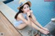 A woman sitting on the edge of a swimming pool wearing a straw hat.
