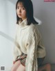 A woman sitting on a bed wearing a white sweater.