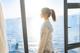 A woman standing in front of a window looking out at the ocean.