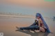 A woman with long blue hair sitting on the beach.