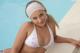 A woman in a white bikini sitting by a pool.