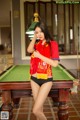 A woman in a red shirt and black panties standing next to a pool table.